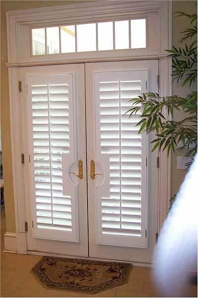 A double entry door with gold fixtures and white custom plantation shutters