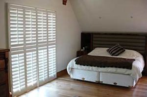 white wood plantation shutters in bedroom with wood foors